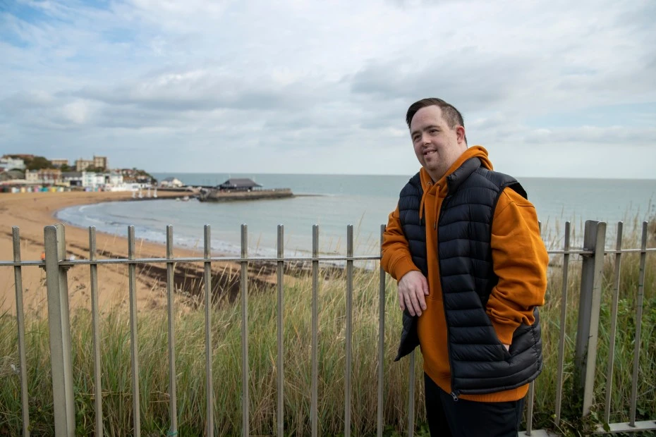 Happy disabled man with down syndrome leaning on fence at beach